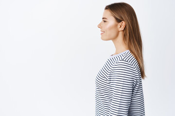 Profile portrait of young blond woman with candid smile, natural light make up, looking left at empty space for chart or product advertisement, white background © Cookie Studio