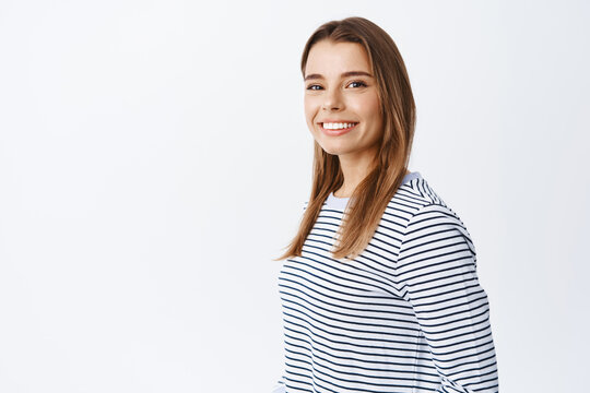 Portrait of young caucasian woman with fair hair and white smile, turn head at camera and looking friendly and natural at camera, standing over white background