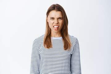 Portrait of disgusted young woman express dislike and disdain, showing tongue and squinting from...