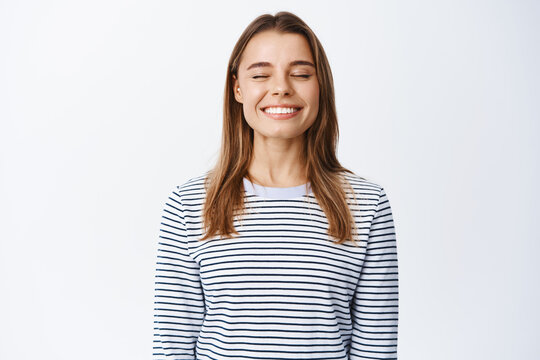 Image of dreamy and happy beautiful woman, close eyes and smiling, breething freely, daydreaming or imaging something positive, standing in casual outfit over white background