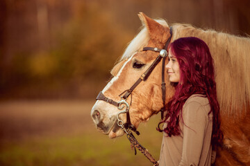 red haired rider and brown horse next to each other look to side on orange pasture field being...