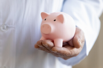 Crop close up of male doctor in white medical uniform hold piggy bank ask about charity donation to hospital. Man GP or therapist offer volunteer contribution or fee to clinic budget. Welfare concept.