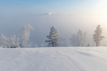 Winter landscape with a view of the city from the hill. The city is hidden under dense fog - 418698515