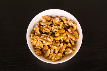 Walnuts, a bunch of peeled walnuts in white bowl on black table top view