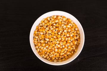 Heap of raw popcorn grains in round white bowl. Dry yellow corns seeds, maize or sweetcorn kernels top view