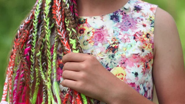 A teenage girl is touching her multi-colored dreadlocks.
