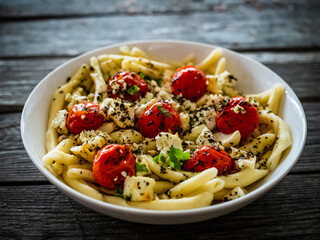 Roasted tomatoes with feta cheese and maccheroni al ferretto served on wooden table
