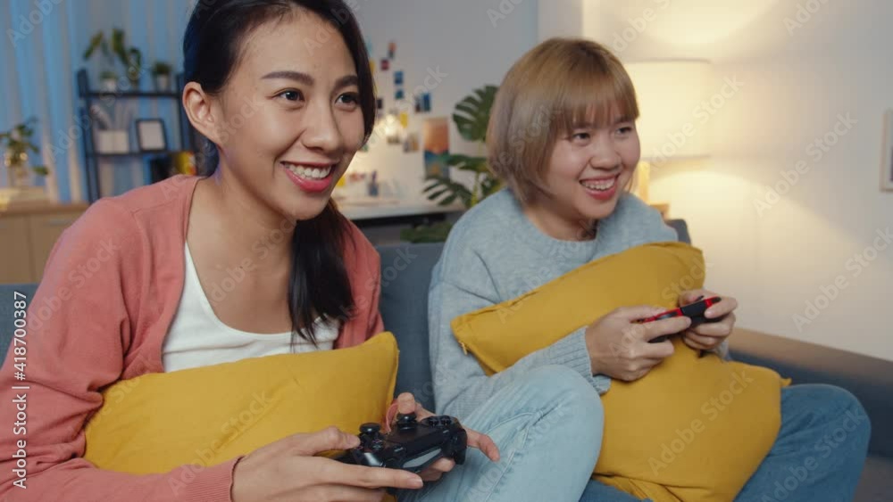 Wall mural lesbian lgbtq women couple play video game at home. young asia lady using wireless controller having