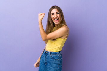 Young woman over isolated purple background celebrating a victory