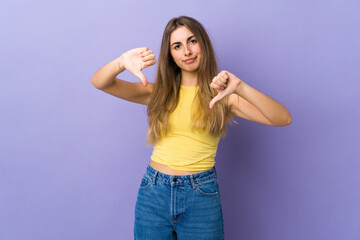 Fototapeta na wymiar Young woman over isolated purple background showing thumb down with two hands