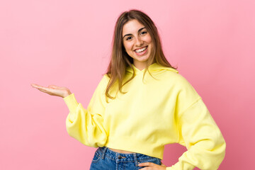 Young woman over isolated pink background presenting an idea while looking smiling towards