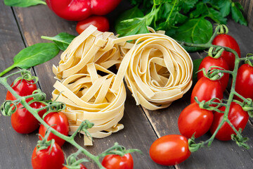 Colorful raw pasta tagliatelle ingredients on wooden table.Closeup view of pasta fresh cherry tomatoes ,spinach and parsley.Vegetables and healthy eating concept.