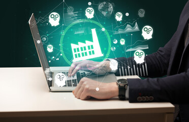 Business hand working on laptop with factory icons coming out from the screen, successful business concept