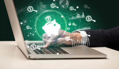 Business hand working on laptop with piggy bank icons coming out from the screen, successful business concept