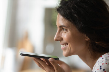 Close up side shot of millennial female face holding smartphone working in loud speaker audio recording mode. Young lady making phone call dialing number using voice recognition technology. Copy space