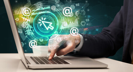 Business hand typing on a modern laptop with cursor icon coming out from multimedia screen, intuitive technology concept