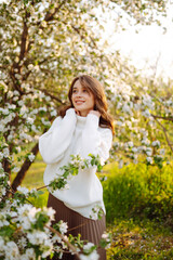 Young woman enjoying scent in blooming spring garden. The concept of youth, love, fashion and lifestyle.