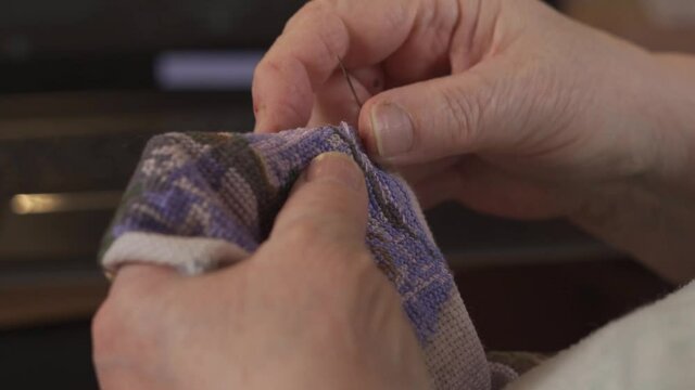The hands of an elderly woman embroider a cross
