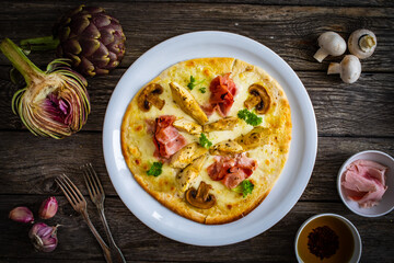 Pizza with artichokes, champignons, ham and mozzarella on wooden background
