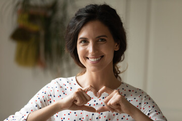 Headshot portrait of smiling woman volunteer social activist look at camera show finger heart draw...
