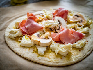 Uncooked pizza with artichokes, champignons, ham and mozzarella on wooden background
