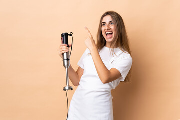 Woman using hand blender over isolated background pointing with the index finger a great idea