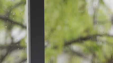 View from indoors on window with rain drops on its glass during cold winter day. Outside trees and branches move as strong winds blow. Storm is coming. Sitting cozy and warm at home looking out - Powered by Adobe