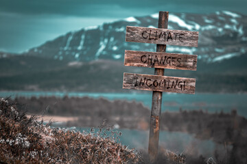 climate changes incoming text quote engraved on wooden signpost outdoors in landscape looking polluted and apocalyptic.