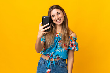 Young woman using mobile phone over isolated yellow background with happy expression