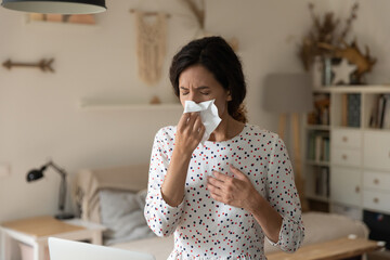 Stay at home. Unhealthy ill young female sneeze wipe blow nose with paper tissue suffer of flu...