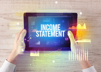 Close-up of hands holding tablet with INCOME STATEMENT inscription, modern business concept