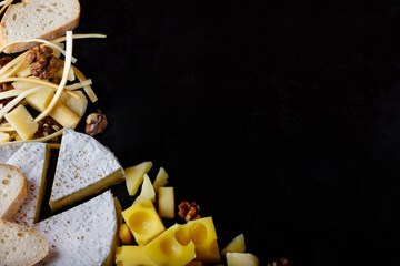 Assortment of cheeses and walnuts on a black table. Top view. Space for you text.