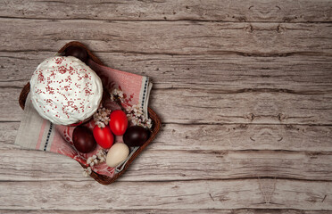 Easter composition. Painted eggs, apricot flowers and a glazed Easter cake on a linen napkin in a basket on a wooden background. Happy Easter Holidays. Top view. Free space.
