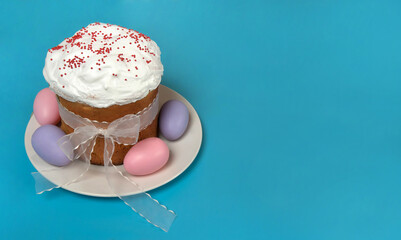 Easter composition. Eggs and a glazed Easter cake with red sugar sprinkles stand on a white plate in close-up on a blue background. Happy Easter Holidays. Free space.