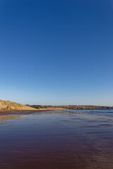 Looking North along the southern Section of Lunan Bay Beach with the tide receeding across the wet sand and a deep blue sky above.