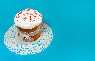 Easter composition. A glazed Easter cake with red sugar sprinkles on a white napkin is depicted in close-up on a pastel blue background. Happy Easter Holidays. Side view. Free space.