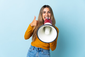 Young hispanic woman over isolated blue background shouting through a megaphone to announce...
