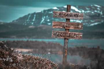 recovery is possible text quote engraved on wooden signpost outdoors in landscape looking polluted and apocalyptic.