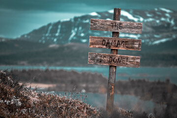 the damage is done text quote engraved on wooden signpost outdoors in landscape looking polluted and apocalyptic.