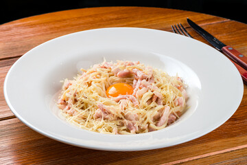 Pasta Carbonara on white plate with parmesan and yolk on dark background