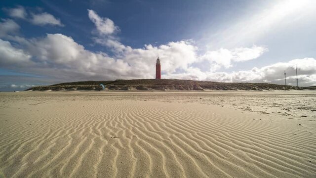 4k time lapse of the Texel lighthouse with wavy sand texture on the beach, white clouds passing by with blue sky background