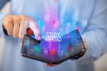 Young man holding a foldable smartphone with STUDY ABROAD inscription, educational concept