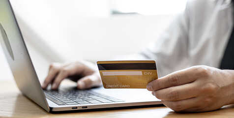 A guy holds a credit card and is filling out his credit card information on his laptop to place an order on the website. Credit cards can be used to pay for goods or services with online merchants.