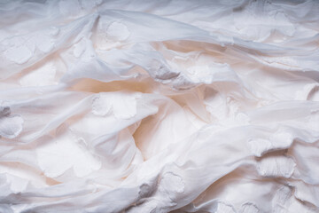 White crumpled cotton fabric. White texture with flowers. Highly detailed closeup of crumpled textile.