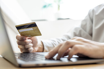 Man holding a credit card and filling out his credit card information on his laptop. Credit cards can be paid for goods and services through general merchants or online stores. Credit card concept.