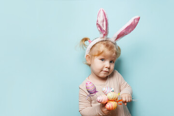 Obraz na płótnie Canvas Portrait of a cute little girl dressed in Easter bunny ears holding colorful egg on blue background