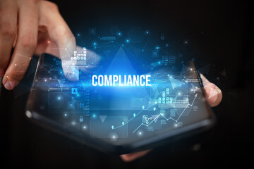 Businessman holding a foldable smartphone with COMPLIANCE inscription, business concept