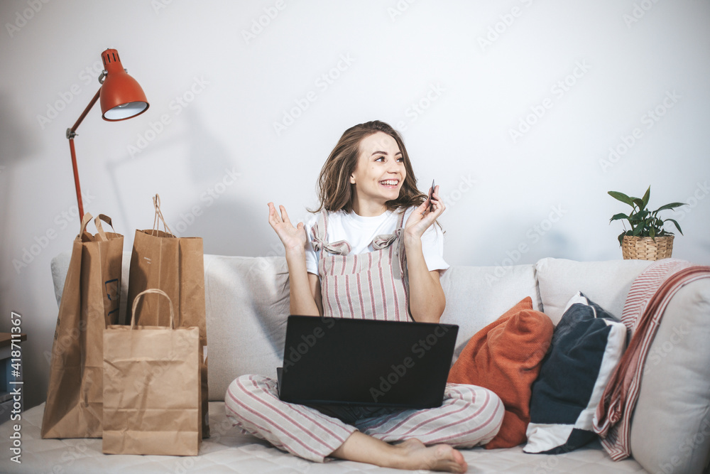 Wall mural young millennial woman shopping online at home. female person using laptop and credit card to buy ne