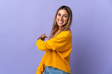 Young hispanic woman over isolated purple background pointing back