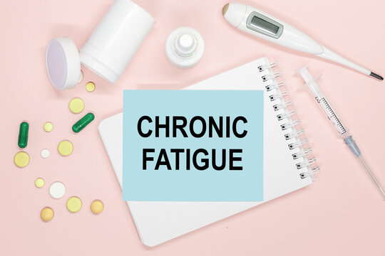 Notebook page with text CHRONIC FATIGUE on a table, pills and syringe. Medical concept.